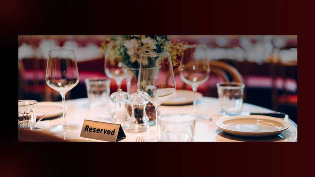 Restaurant table setting with 'Reserved' sign, wine glasses, plates, salt & pepper shakers, and floral centerpiece.