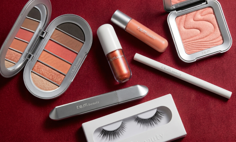 | r.e.m. beauty Review 2026: Is Ariana Grande’s Brand Worth It? An open silver r.e.m. beauty eyeshadow palette resting next to a white tube concealer lip gloss balm and a pressed pink blush compact