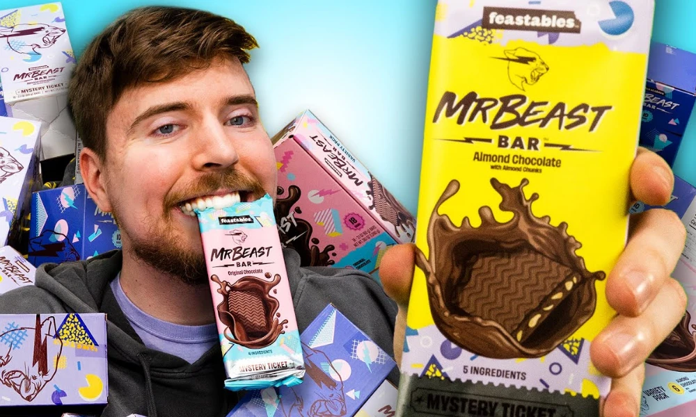 | Feastables: MrBeast's $250M Chocolate Empire & Why It's More Profitable Than YouTube Close up of MrBeast holding an official yellow Feastables Almond Chocolate bar package