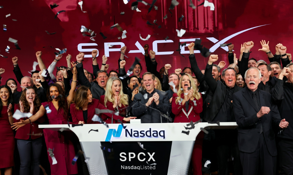 | Elon Musk's SpaceX Begins Trading in Record-Breaking IPO: The Complete $75 Billion Deep Dive (2026) Elon Musk speaking at the Nasdaq stock market podium screen display with the corporate SpaceX logo