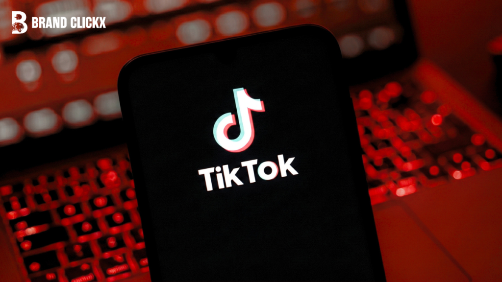 Feature – TikTok AI Creative Studio 2026 A smartphone screen displaying the official TikTok logo against a dark red illuminated mechanical keyboard background by BrandClickX