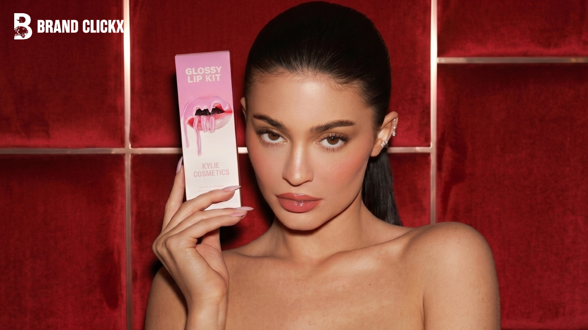 Kylie Cosmetics Lip Kit A promotional beauty portrait of Kylie Jenner holding a pink Glossy Lip Kit packaging box against a dark red velvet backdrop by BrandClickX