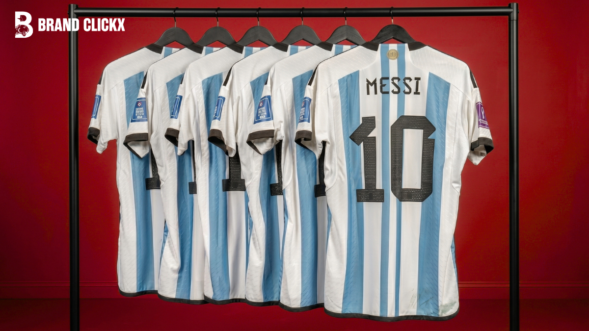Multiple soccer jerseys hanging on clean wooden hangers against a seamless solid blue studio backdrop