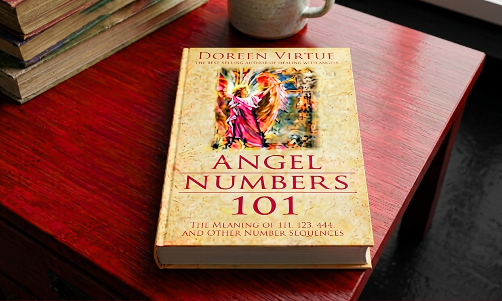 | Angel Numbers: The Complete Guide to Meaning, Numerology, and Spiritual Messages (2026) The book cover of Angel Numbers 101 by Doreen Virtue resting on a dark red polished wooden table