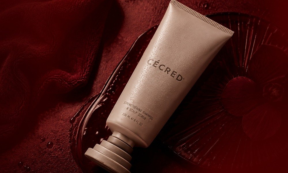 | Cécred Hair Products Review: Beyoncé's Complete 2026 Guide An elegant matte beige bottle of Cécred Moisture Sealing Lotion with a unique spherical cap resting on a dark red stone slab