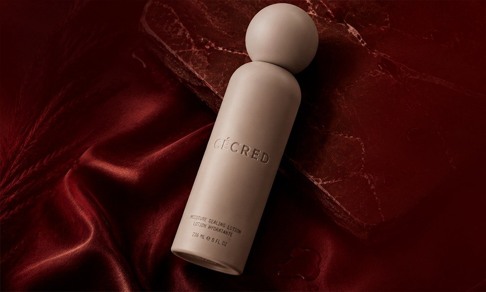 | Cécred Hair Products Review: Beyoncé's Complete 2026 Guide A close-up view of a wet beige squeeze tube of Cécred Strengthening Shampoo and Scalp Scrub on a deep red satin background