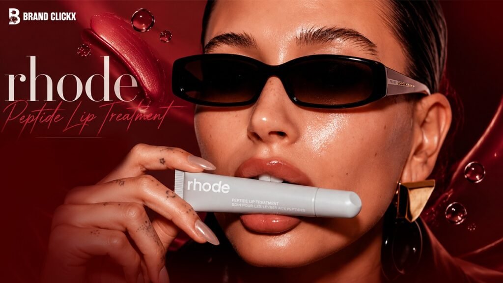 hailey-bieber-rhode-peptide-lip-treatment-editorial An official close-up promotional portrait of Hailey Bieber wearing sunglasses and holding a tube of Rhode Peptide Lip Treatment in her teeth