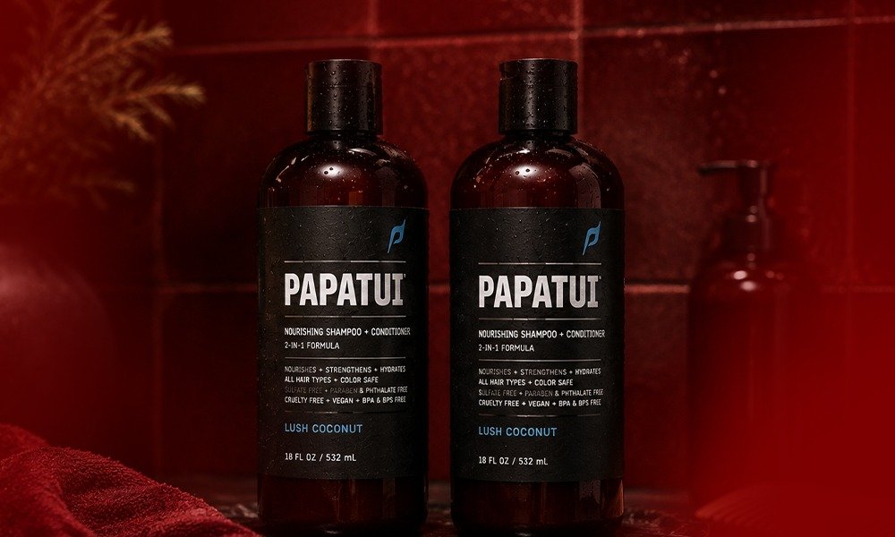 | Papatui Review: Testing Dwayne "The Rock" Johnson's Men's Care Brand Two bottles of Papatui Nourishing Shampoo and Conditioner 2-in-1 in Lush Coconut flavor placed against a textured dark red background