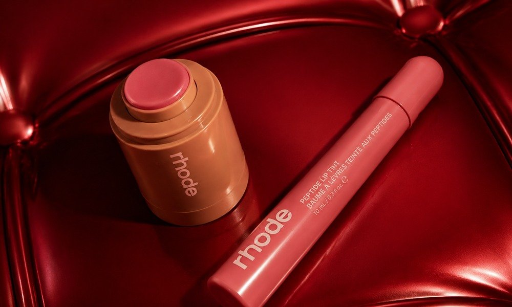 | Rhode Lip Peptide Treatment Review: Flavors & Buying Guide (2026) An open tube of pink Rhode Pocket Cream Blush resting next to a matching tube of pink Peptide Lip Tint on a red tufted leather surface