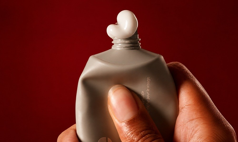 | Rhode Lip Peptide Treatment Review: Flavors & Buying Guide (2026) A close-up view of a hand squeezing a dollop of thick white cream lotion from a gray Rhode skincare tube