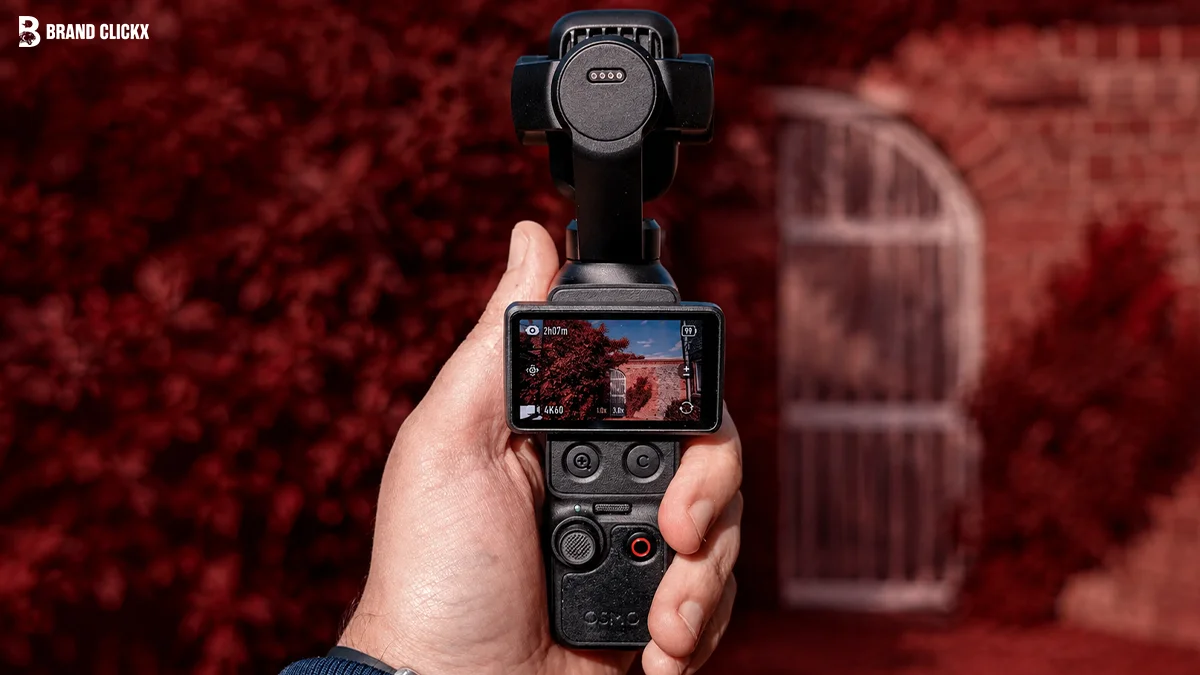 A hand holding a pocket gimbal camera against a deep red background