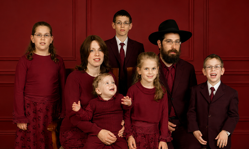 | 150+ Jewish Last Names and Their Origins Explained A family dressed in formal attire posing for a portrait in deep red.