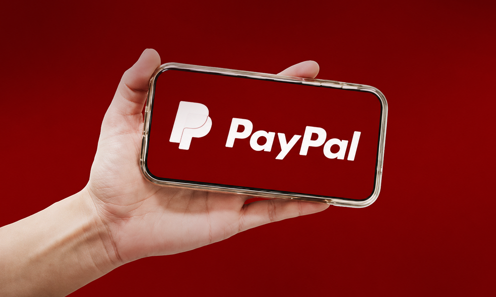 Hand holding a smartphone displaying the PayPal logo
