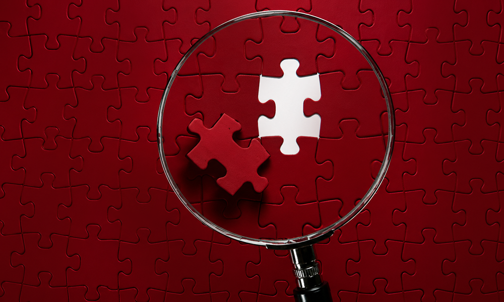 Magnifying glass focusing on two jigsaw puzzle pieces on a red board.
