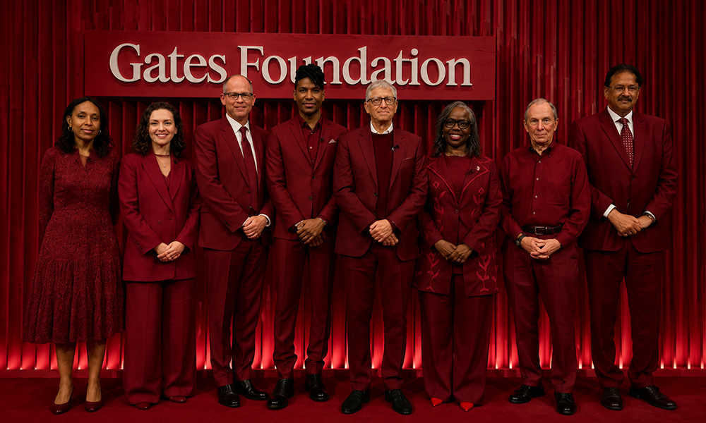 | Warren Buffett Drops Gates Foundation From Annual Donations for First Time in 20 Years Group of people wearing red clothing in front of a Gates Foundation sign.