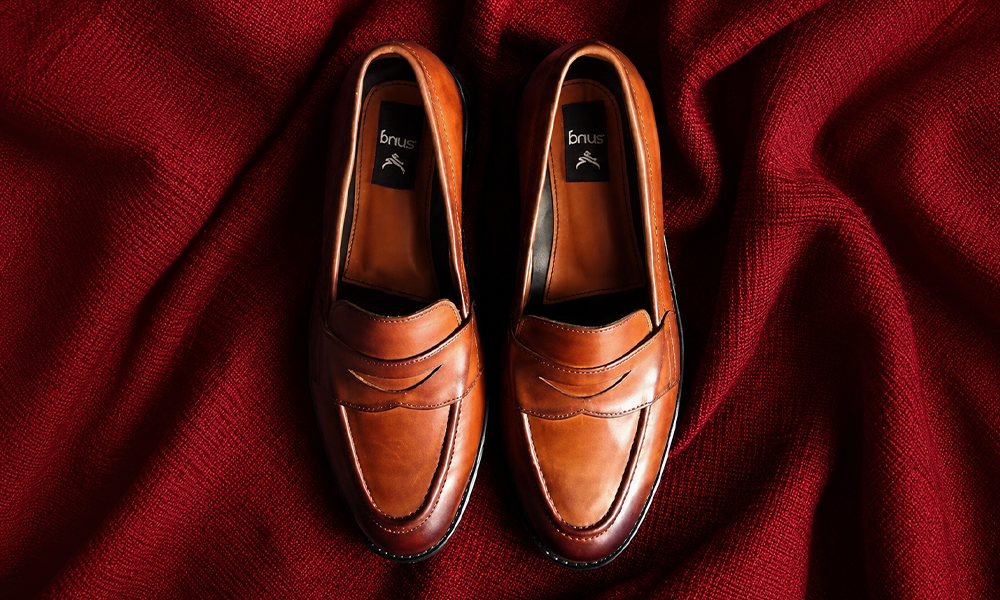 | Penny Loafers: The Complete Buying Guide, Styling Tips & Best Picks (2026) A pair of brown leather loafers displayed on a dark red fabric.