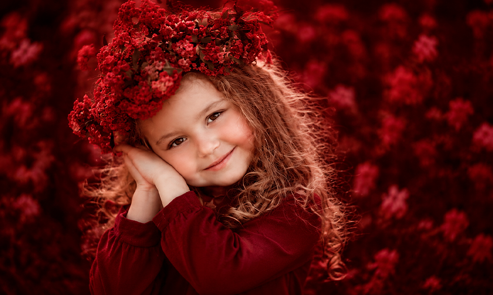 Smiling young girl with curly hair wearing a red floral wreath.