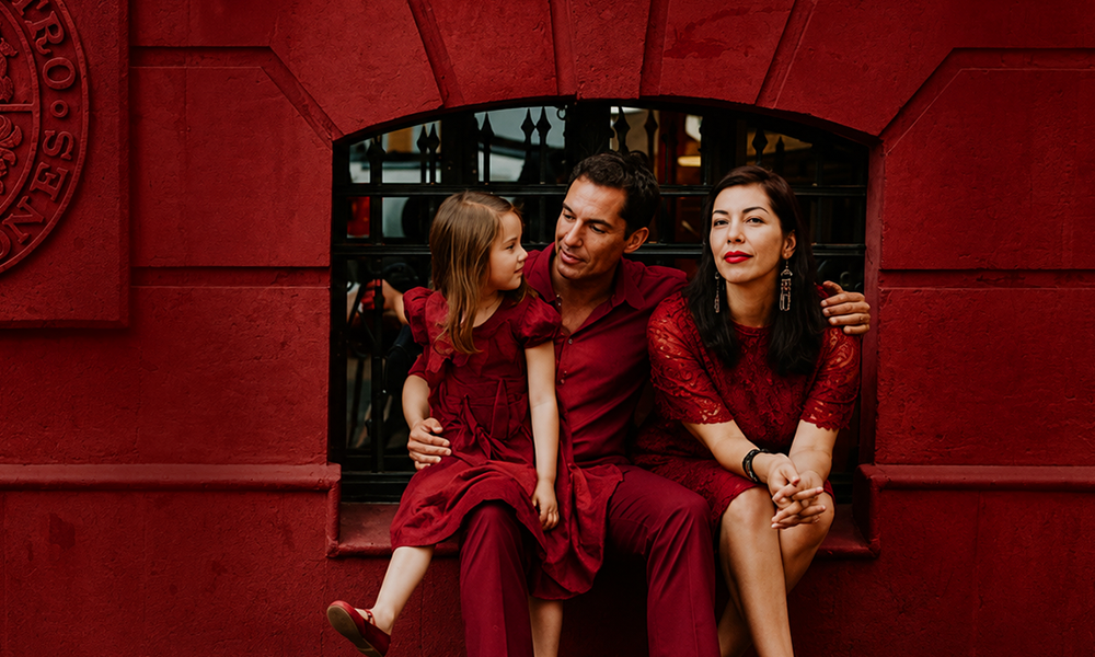 A family in red clothing posing together against a matching red wall.
