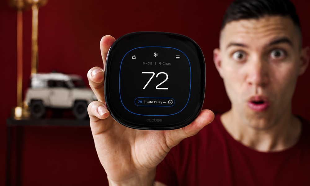 A person holding up a smart thermostat displaying temperature settings in a modern room setup