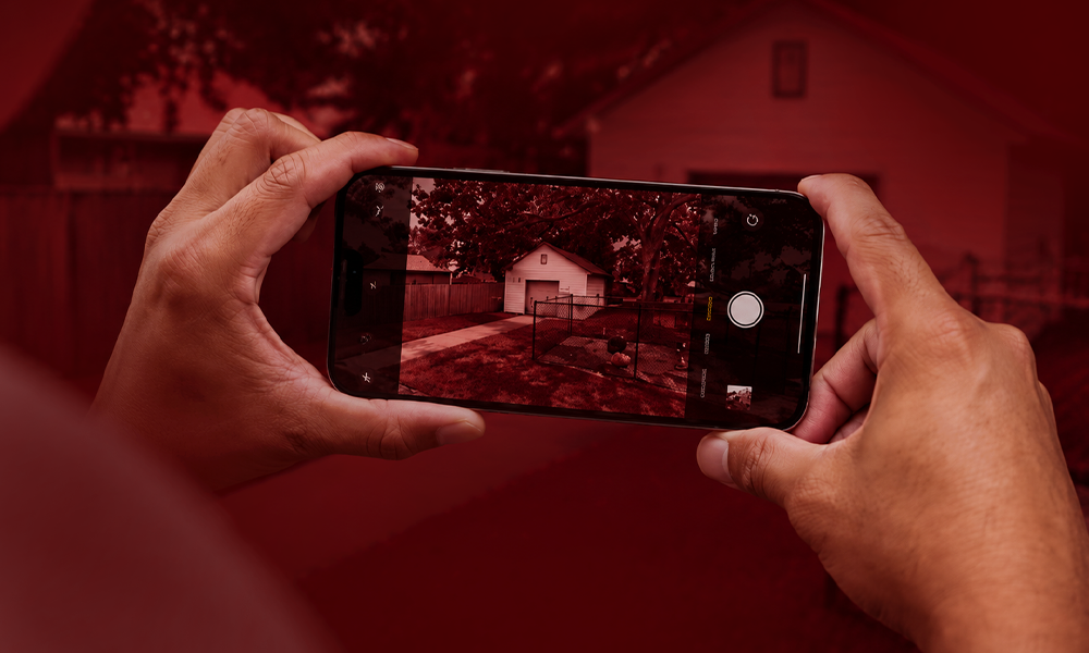 | Hidden iPhone Camera Tricks You Should Start Using Right Now Person holding a smartphone in a shooting pose against a deep red backdrop.