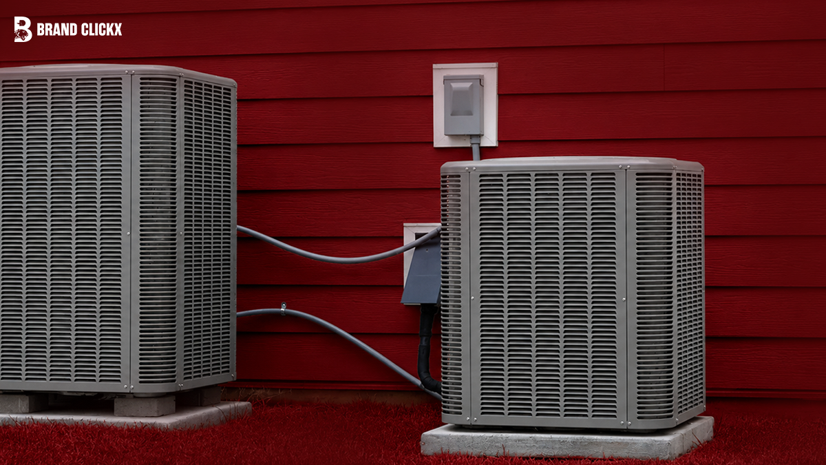 Two outdoor HVAC compressor units installed next to a red wall.