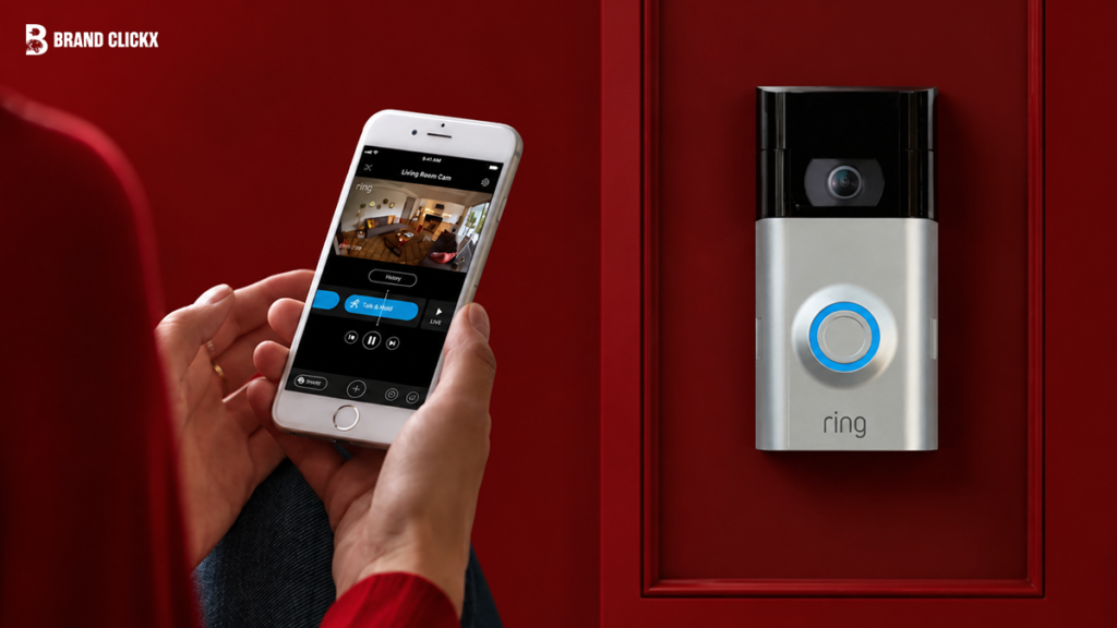 Hands holding a smartphone showing a video doorbell live feed app interface next to the installed device on a red wall