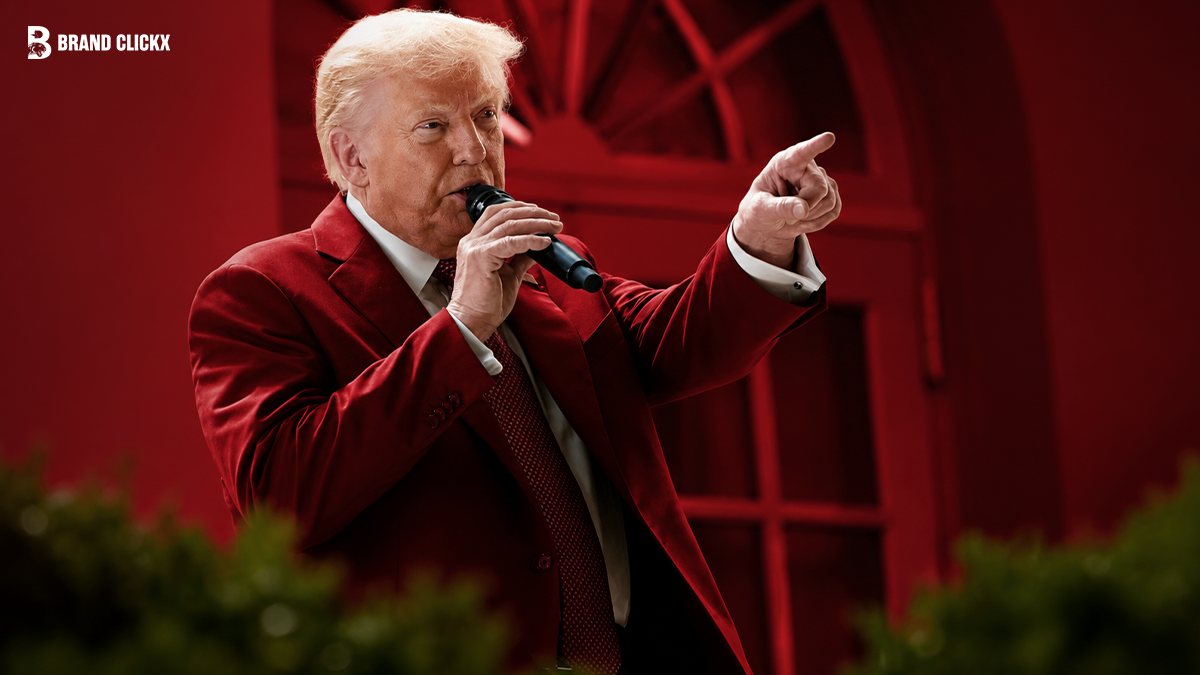 Donald Trump speaking into a microphone and pointing forward wearing a red suit and red tie in front of a red doorway