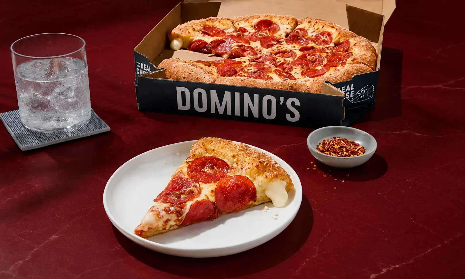 | Domino's Pizza: Menu, Deals & Order Online 2026 A single slice of pizza on a white plate with dipping sauce under red ambient light