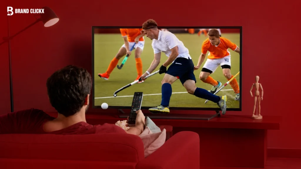 A person watching a live sports broadcast on a TV screen in a room with a red ambiance.