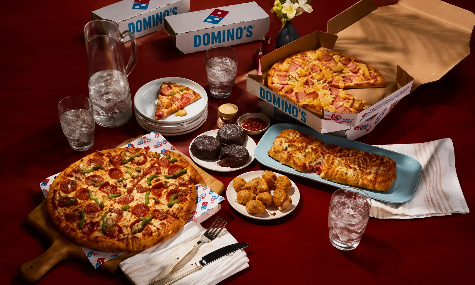 | Domino's Pizza: Menu, Deals & Order Online 2026 Assorted Domino's menu items spread across a dark red table setting