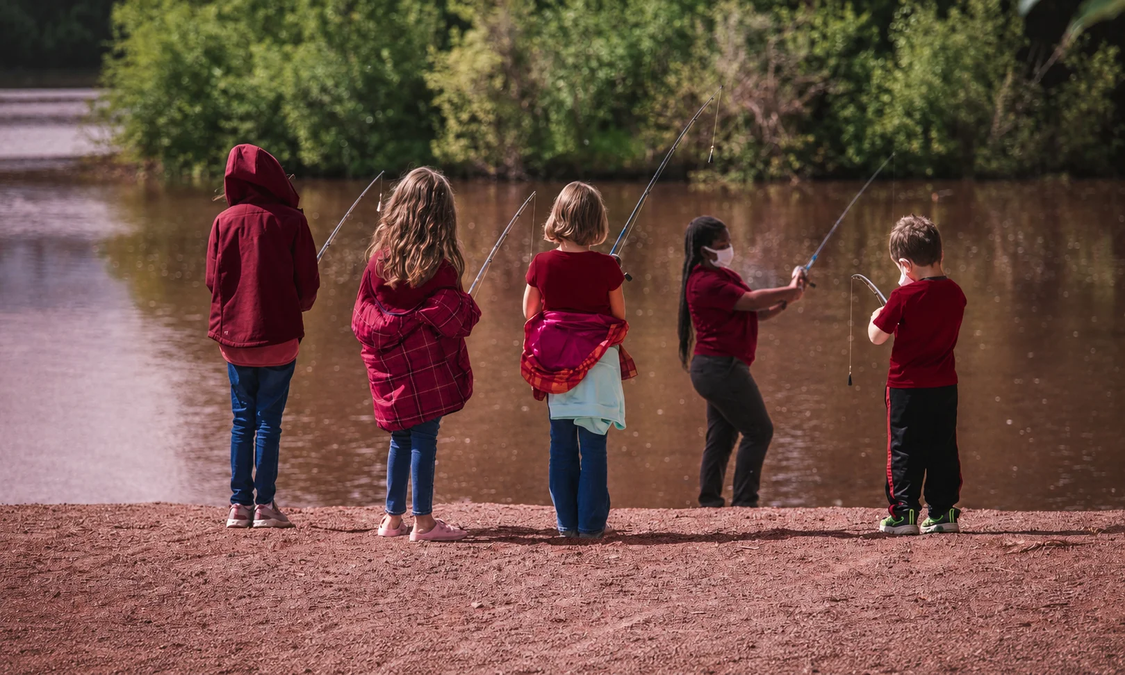 | Academy Sports 2026: Hours, Deals, Locations & More People standing outdoors near a lake shore in a red-toned landscape setting