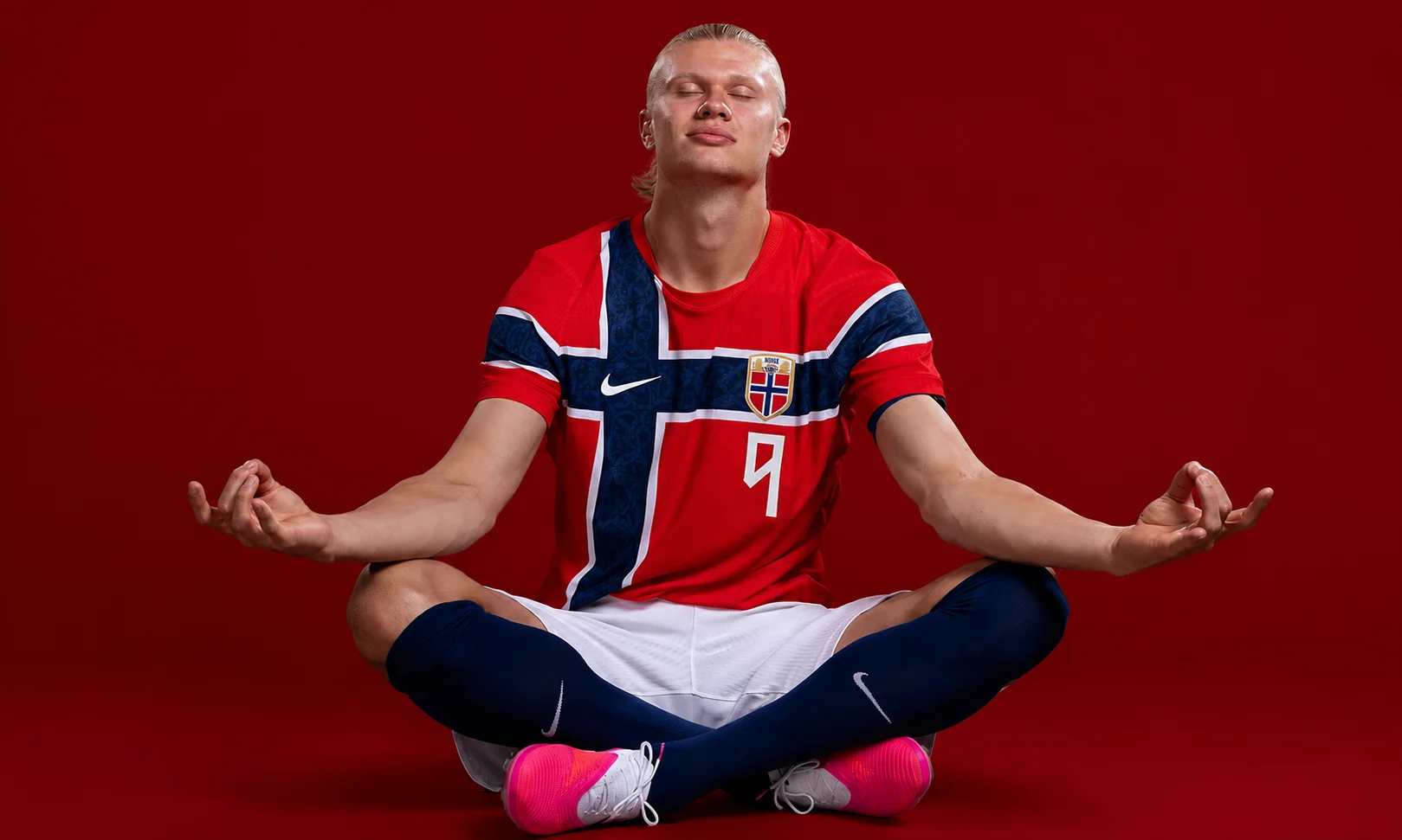 Person sitting in a meditative pose wearing a Norwegian jersey on a red background