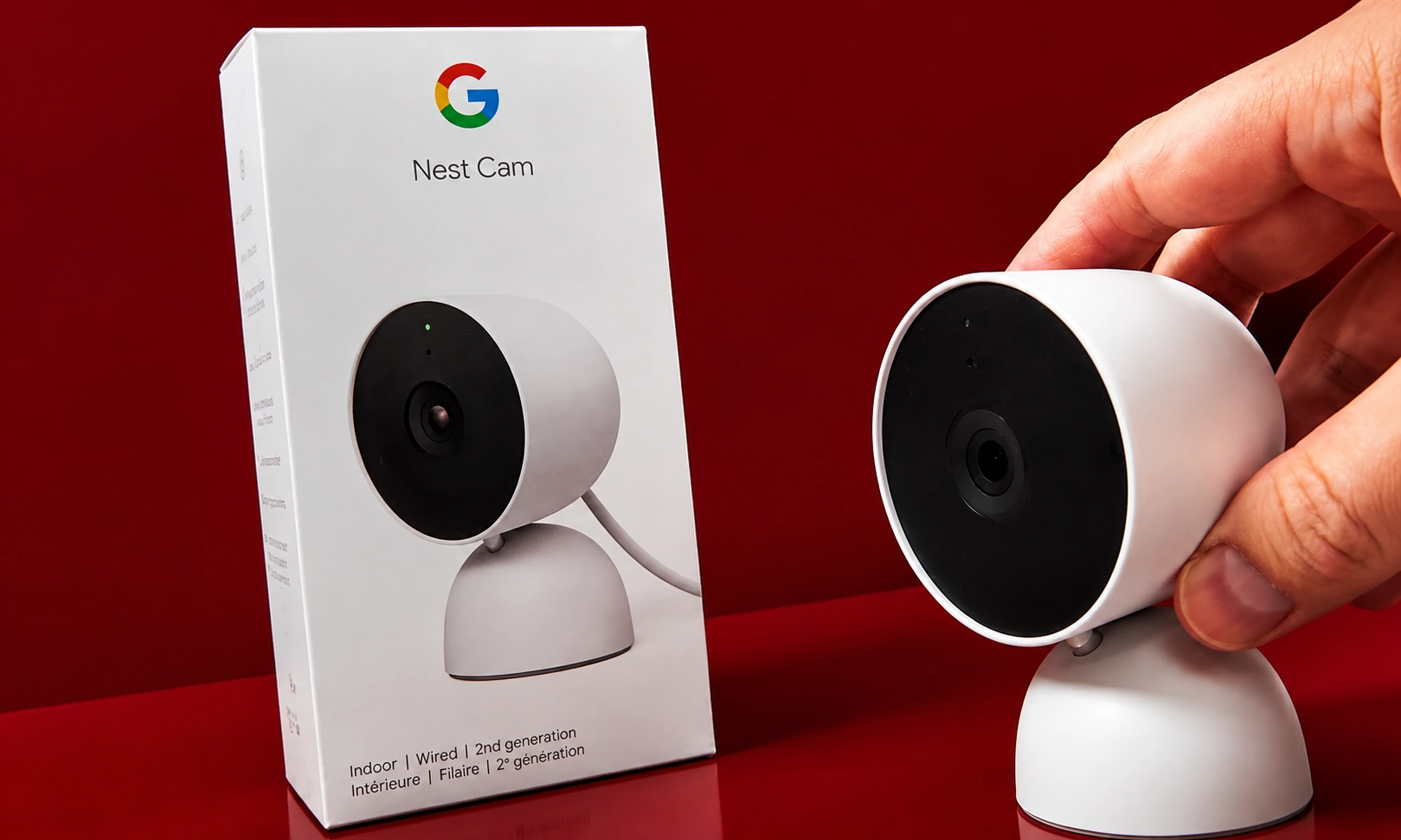 A hand holding up a white smart security camera next to its product box.
