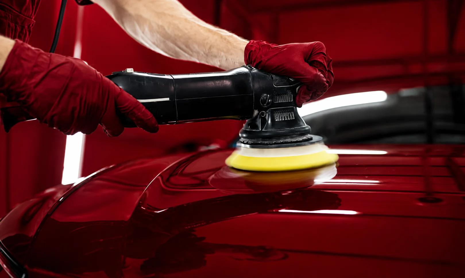 Close-up of hands detailing a vehicle finish under rich dark red lighting