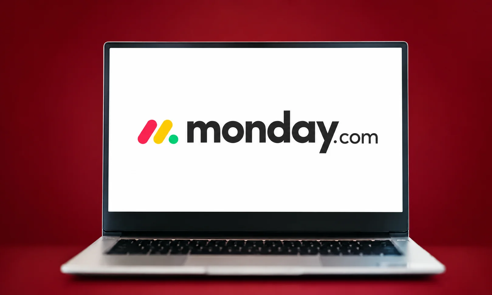 Monday.com workflow management board displayed on a laptop in a red-themed setting