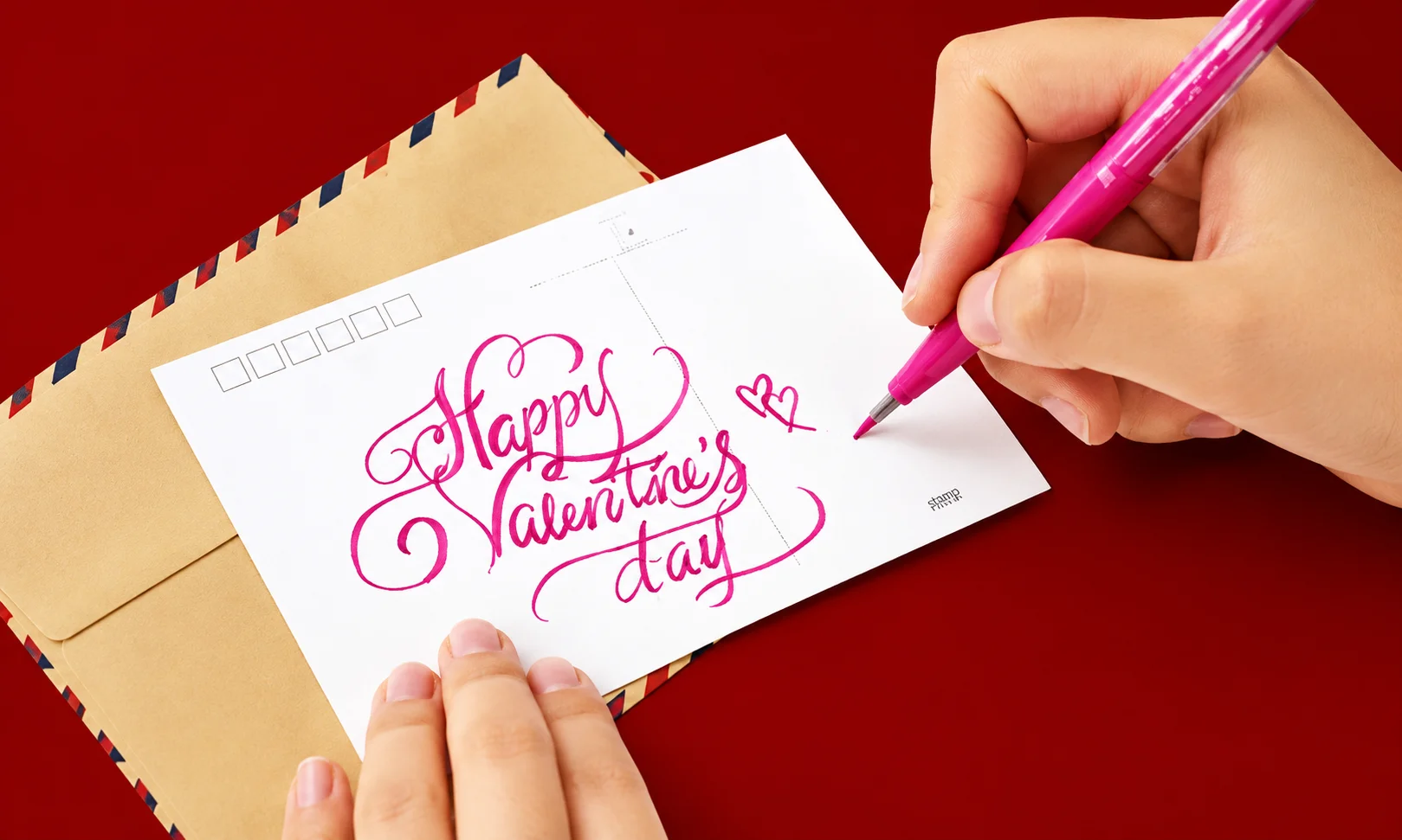 Person practicing calligraphy and hand lettering with a pink pen on paper against a dark red background