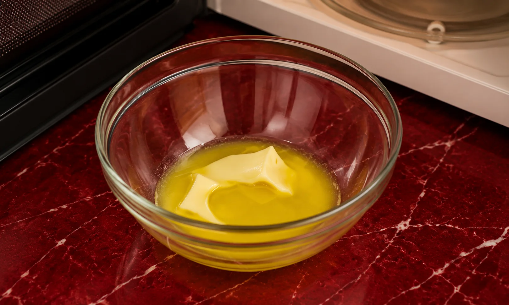 Melted butter inside a clear glass bowl displayed against a rich red studio backdrop.