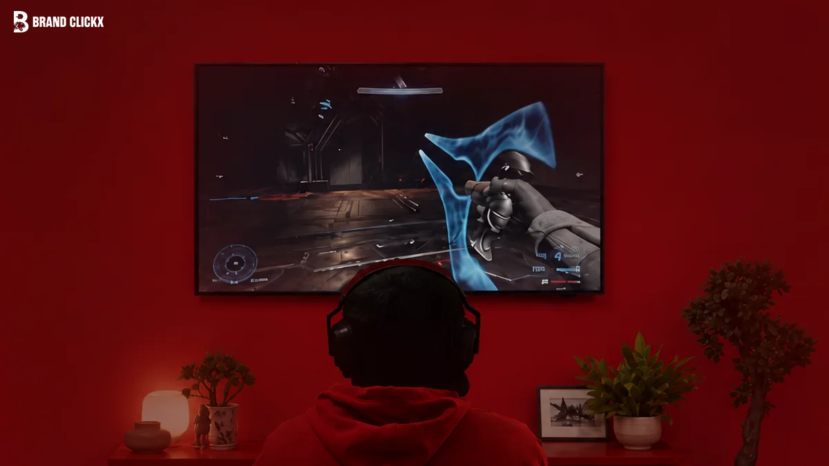 Gamer wearing a red hoodie and headphones playing a sci-fi game on a large wall-mounted screen against a red wall