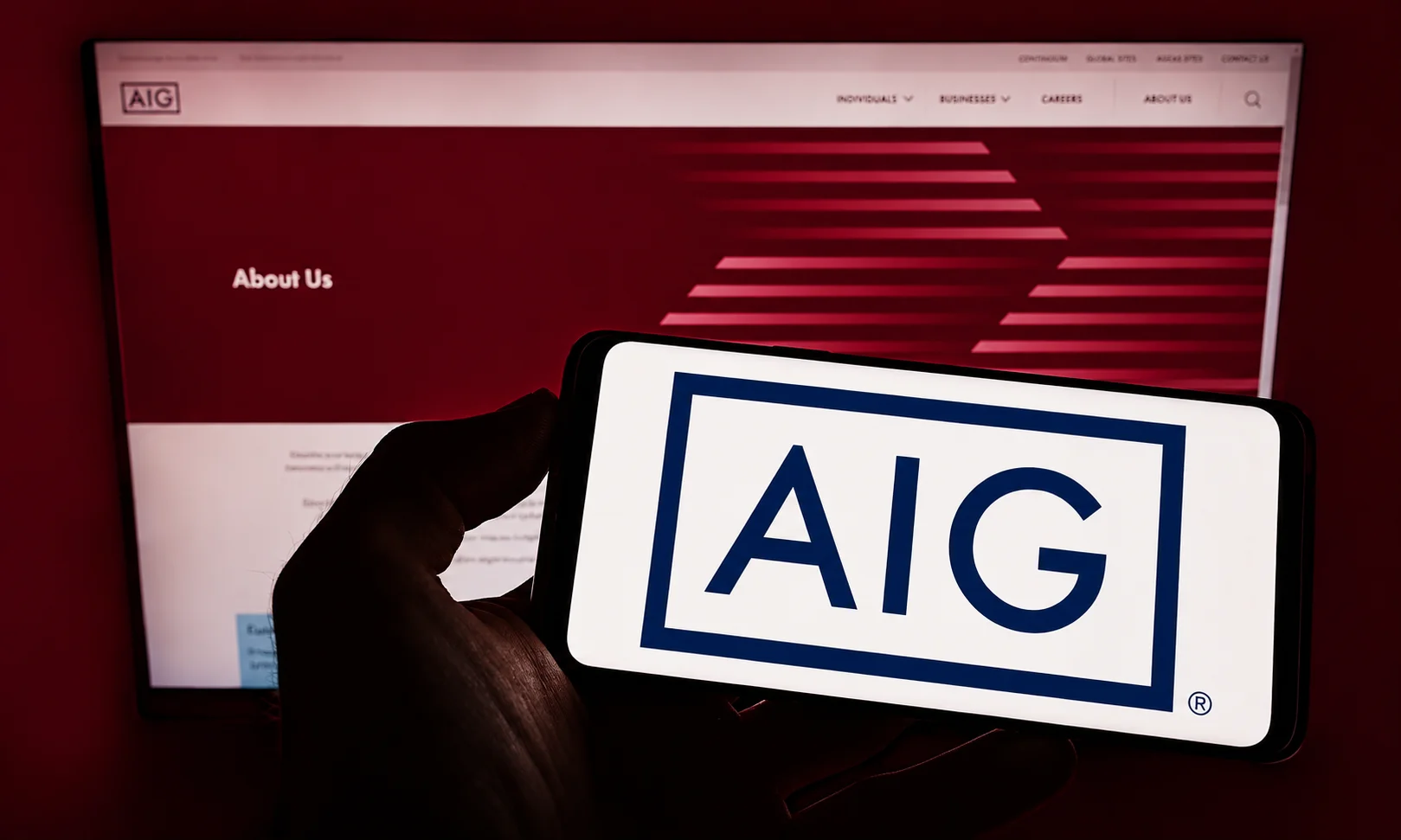 | Best Insurance Companies in the World in 2026 A hand holding a smartphone displaying the AIG insurance company logo in front of a website screen.