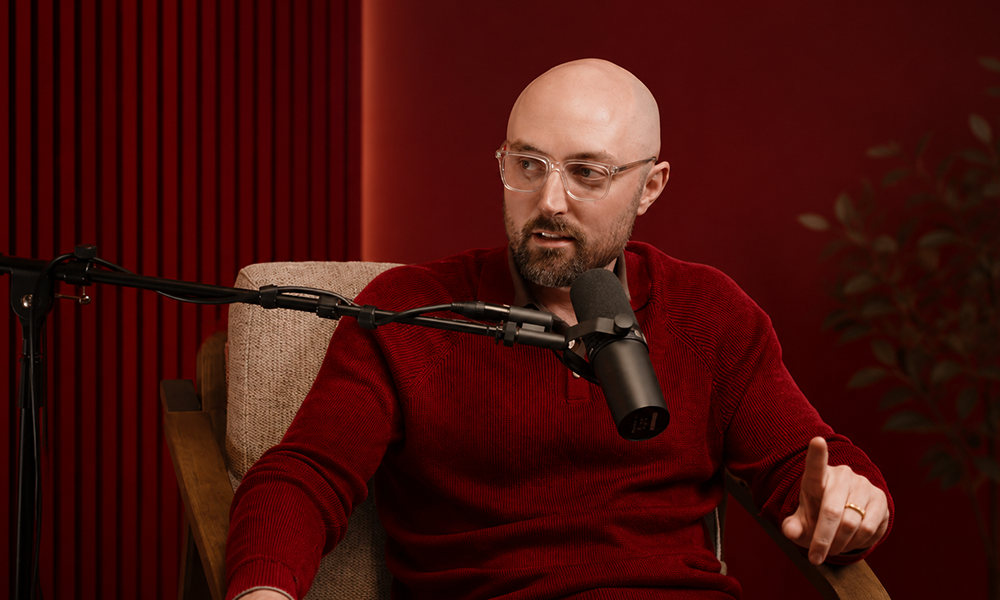 Man wearing a red sweater sitting in a studio with a warm, dark red ambient background