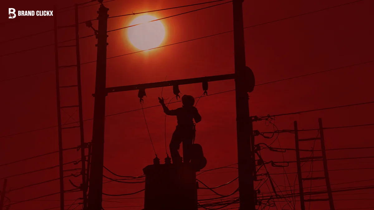 Silhouetted linesman working on power poles against a glowing red sky