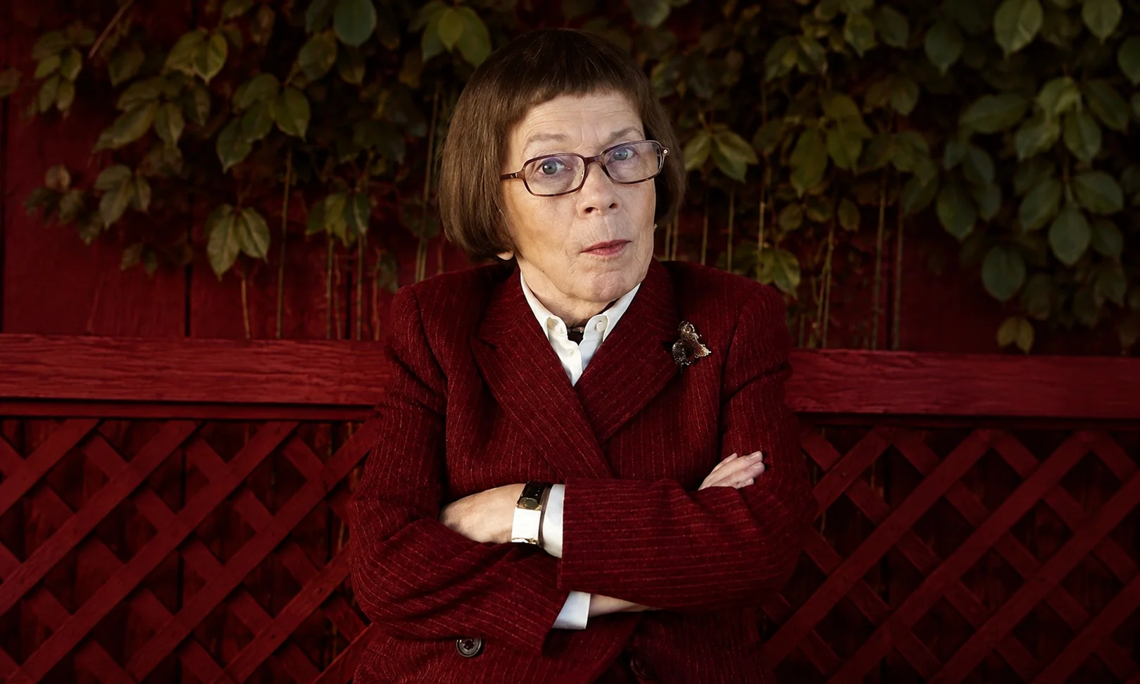 Portrait of a person with crossed arms set against a dark red studio background.