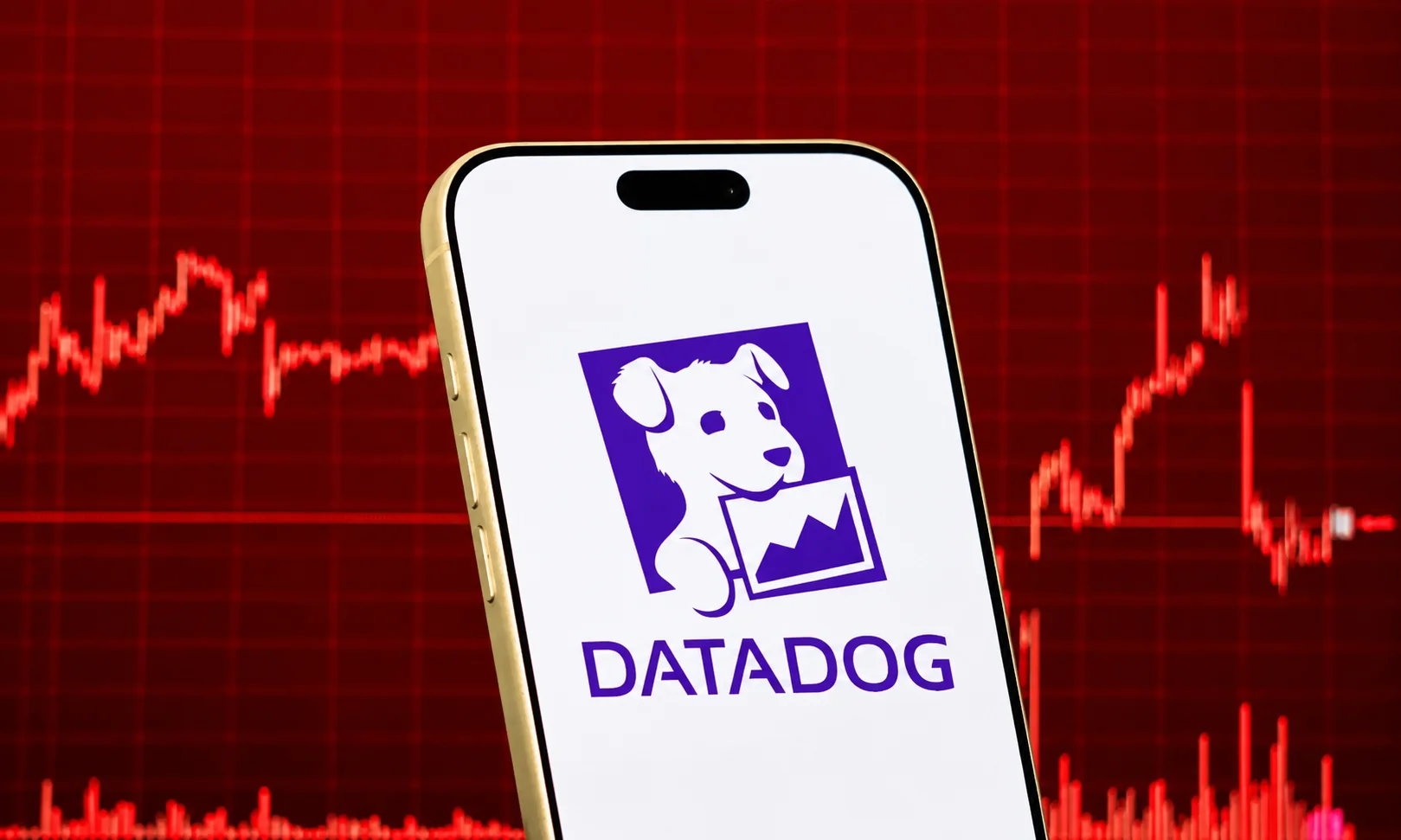 A smartphone displaying the Datadog logo with red financial market trading graphs in the background.