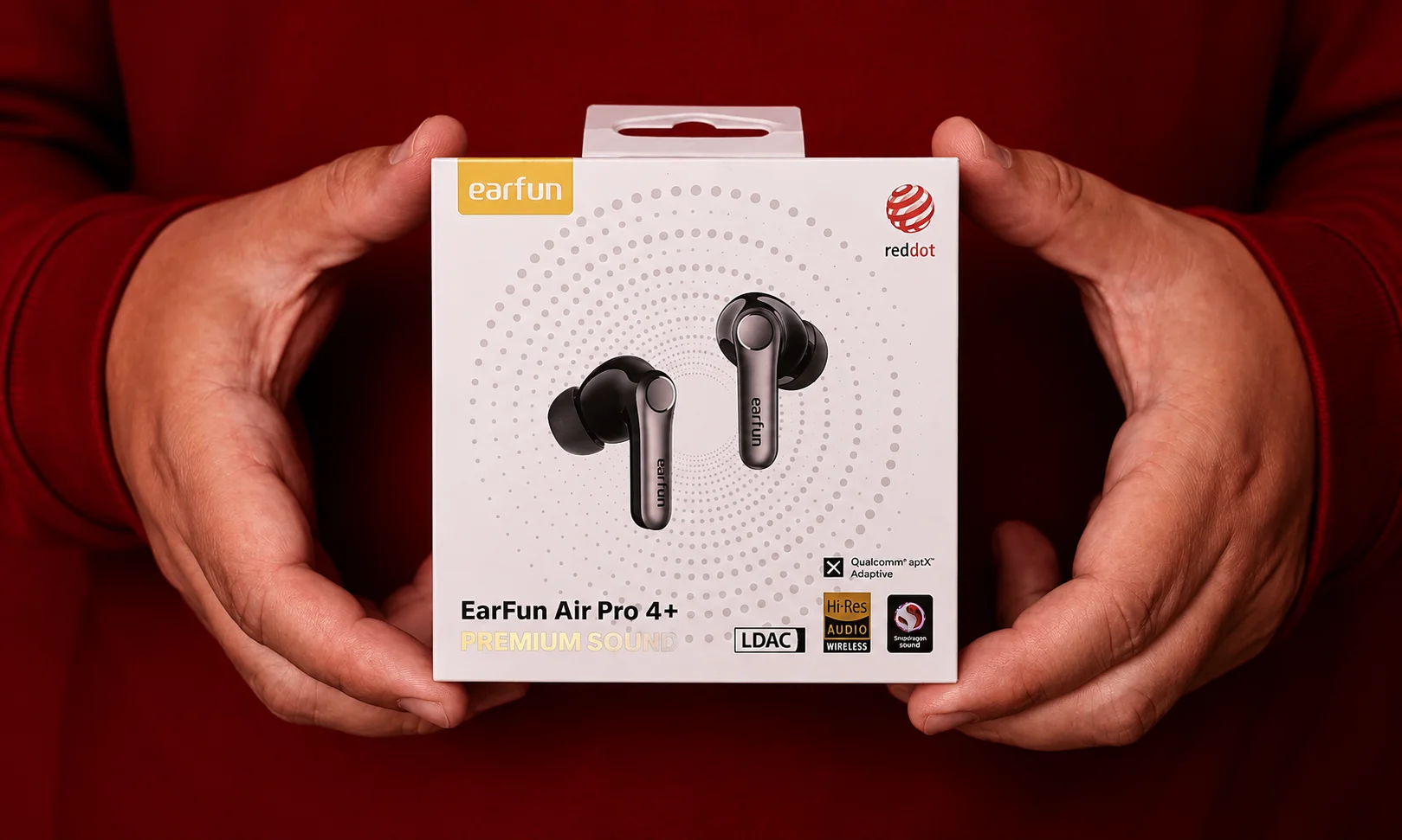 A pair of EarFun earbuds held in hands against a dark red background.