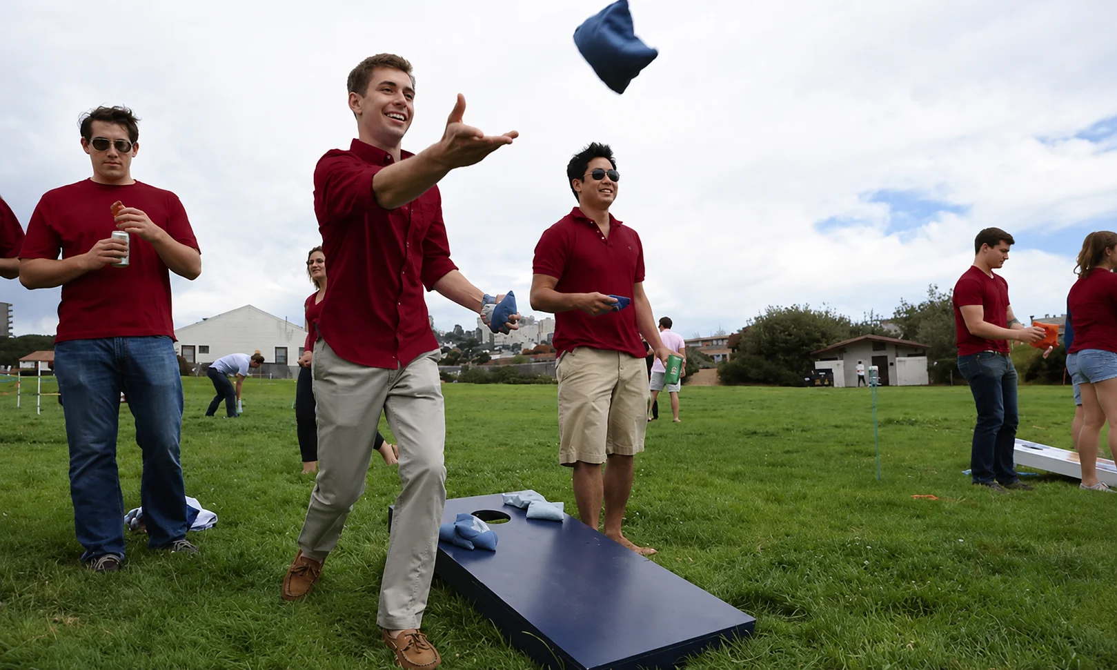 Player aiming and throwing a cornhole bag towards the wooden board during a backyard game.