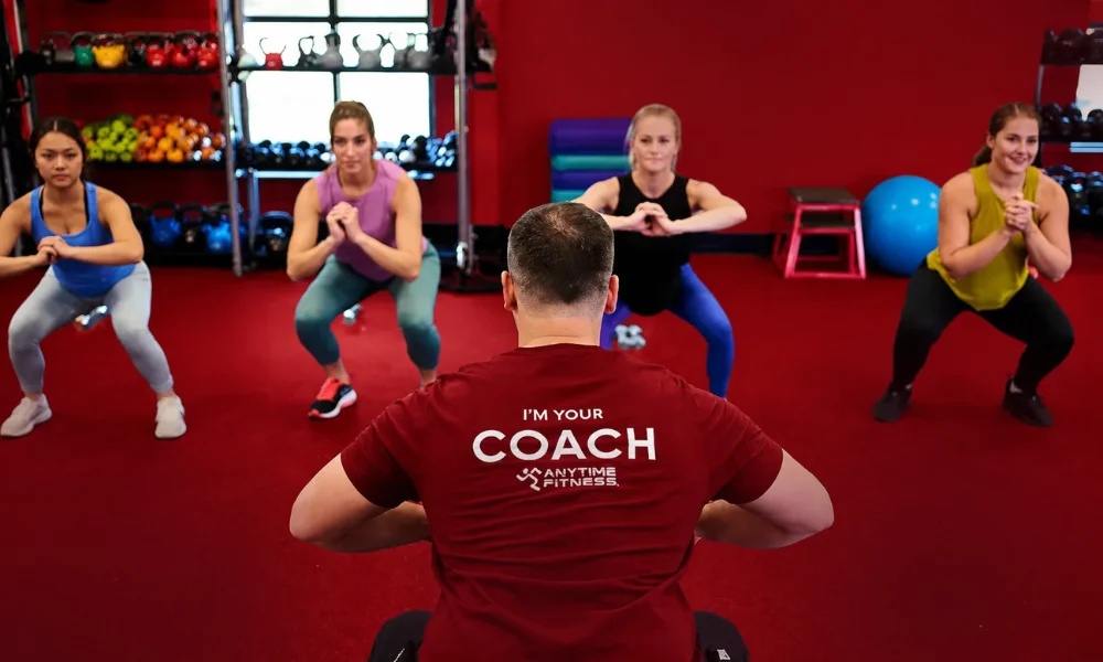 Fitness coach leading a workout session for men in a gym with a dark red background