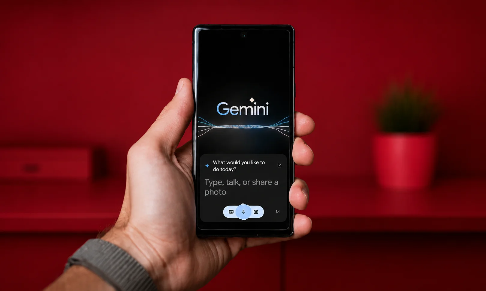Hand holding a smartphone displaying the Gemini app interface on a red-themed desk