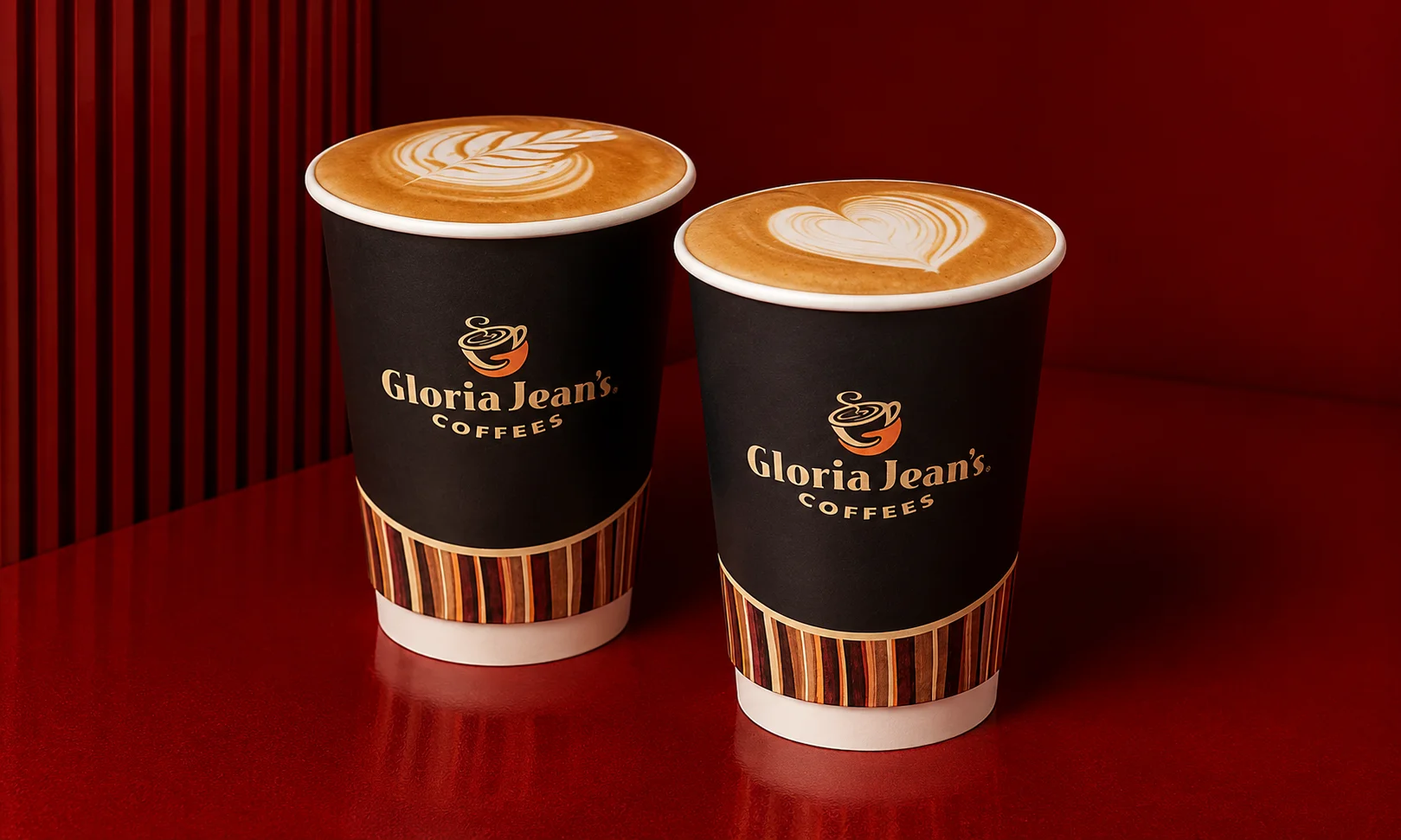 Gloria Jeans branded coffee cups placed on a wooden surface.