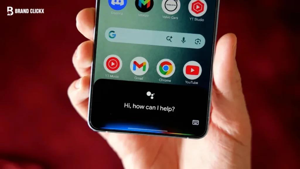 Hands holding a smartphone displaying the Google Assistant interface against a rich dark red background
