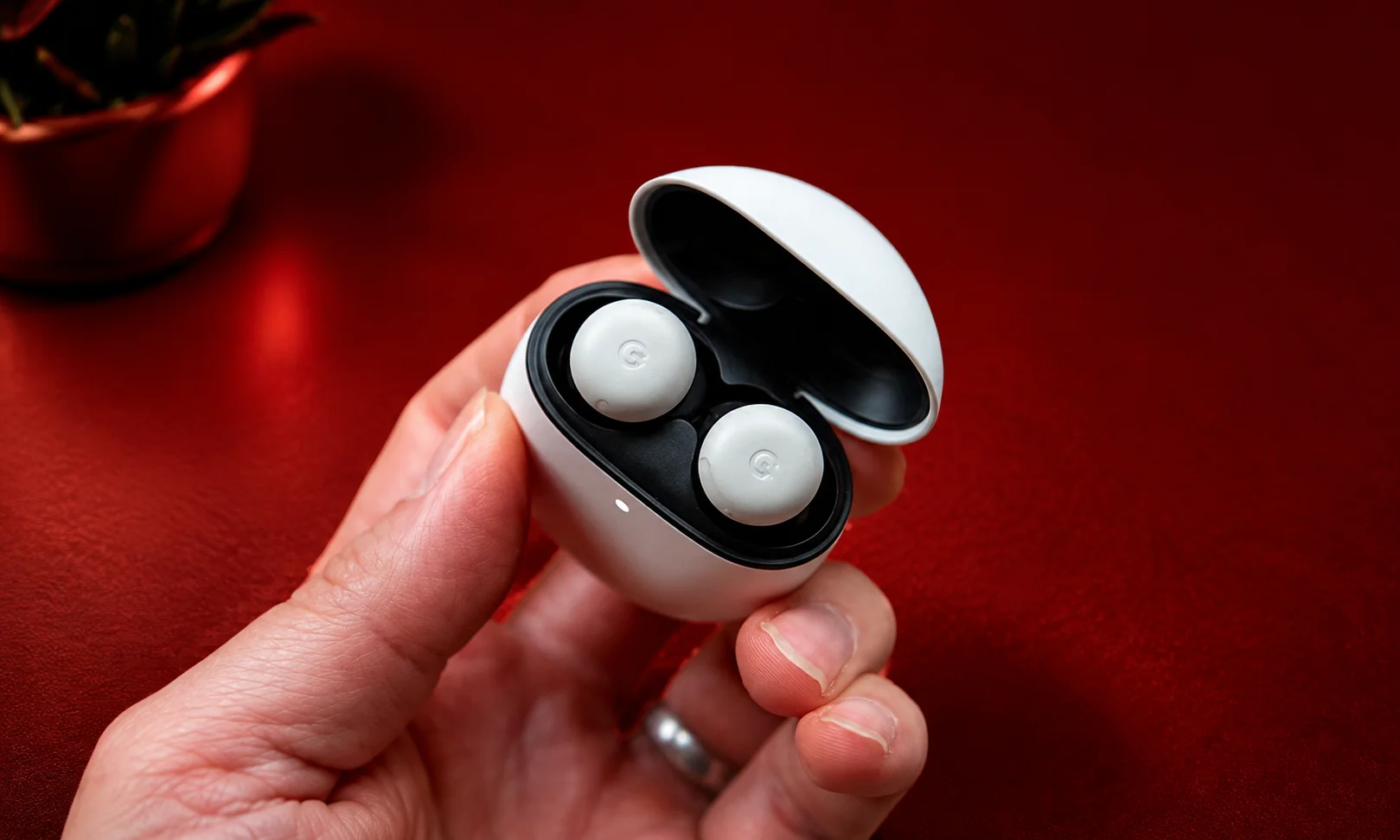 A hand holding Google Pixel Buds Pro 2 earbuds against a red aesthetic.